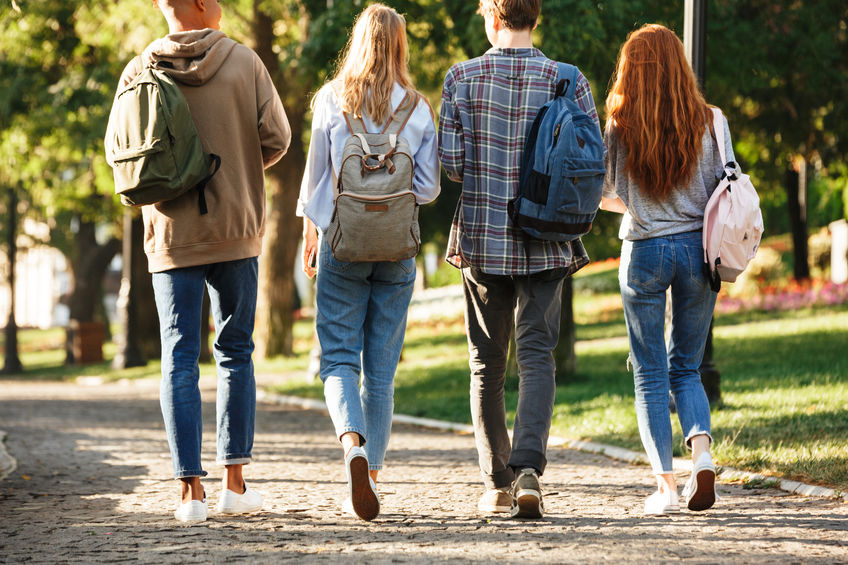 Back view group of students with backpacks walking at the campus outdoors