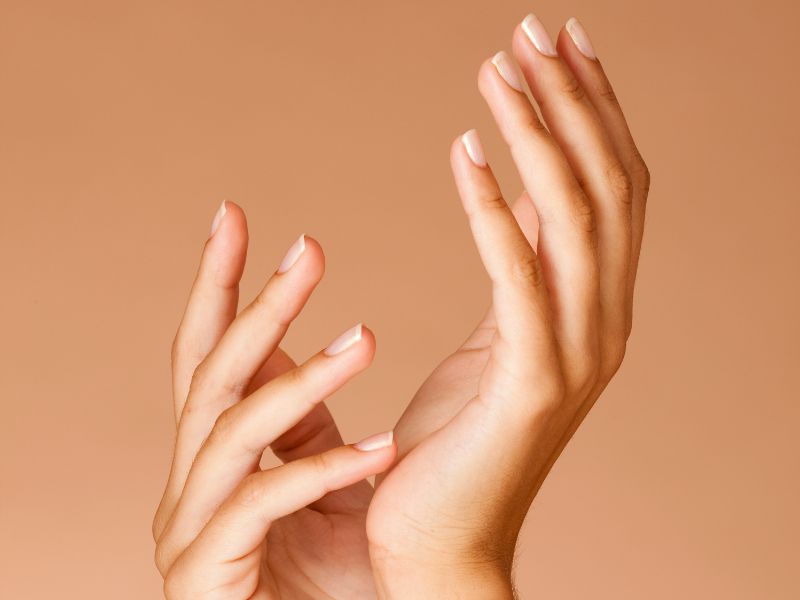 Two hands with neatly manicured nails are held gracefully against a soft beige background.