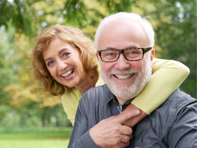 An older woman hugs a smiling older man from behind as they pose outdoors, both appearing happy—like the positive feedback seen in many prostarex™ reviews.