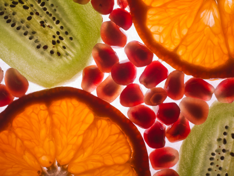 Close-up of sliced kiwi, orange, and pomegranate seeds arranged together, showing vibrant colors and details of the fruit textures.